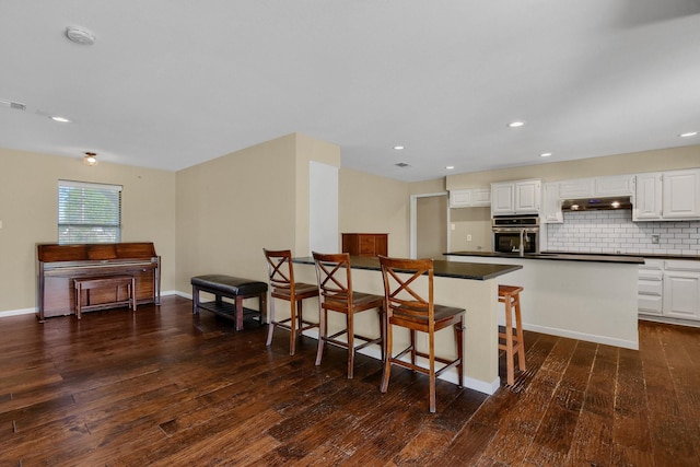 kitchen featuring white cabinetry, a kitchen bar, decorative backsplash, stainless steel oven, and dark wood-type flooring