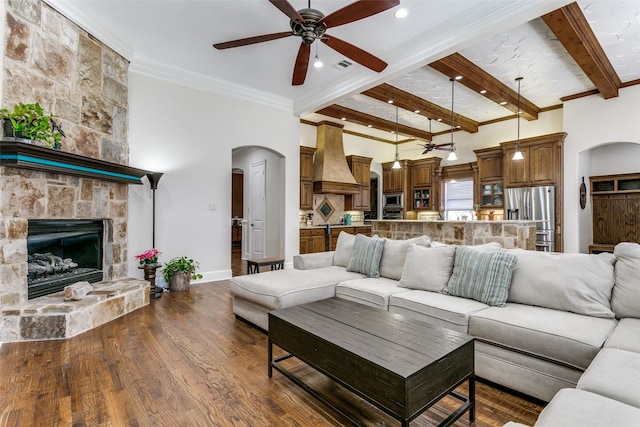 living room featuring ceiling fan, dark hardwood / wood-style flooring, a fireplace, ornamental molding, and beamed ceiling