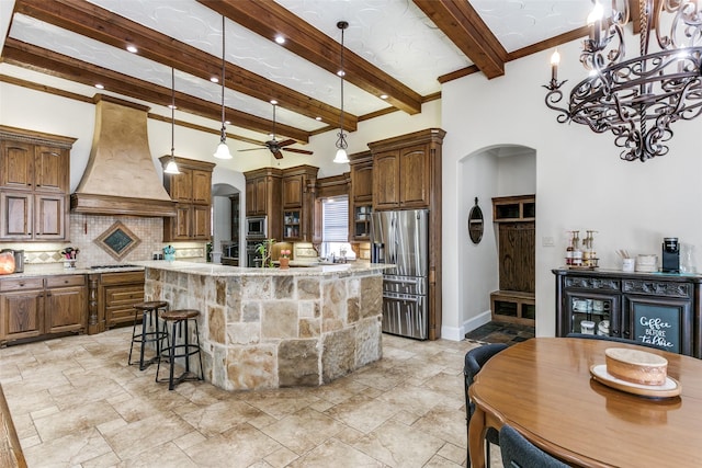 kitchen featuring tasteful backsplash, custom exhaust hood, beam ceiling, appliances with stainless steel finishes, and an island with sink