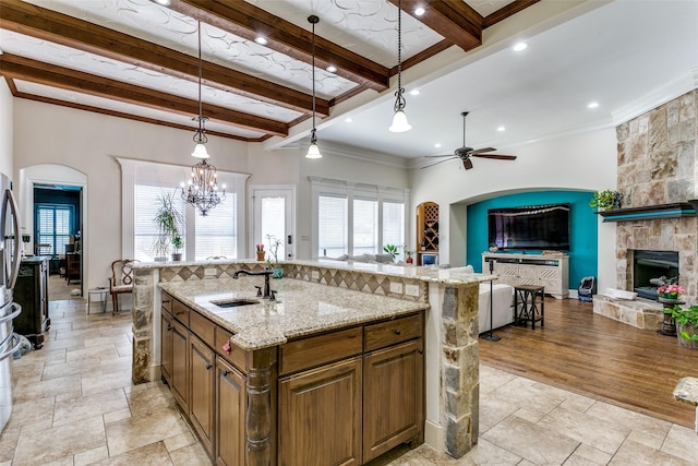 kitchen with ceiling fan with notable chandelier, decorative light fixtures, sink, light stone counters, and a center island with sink