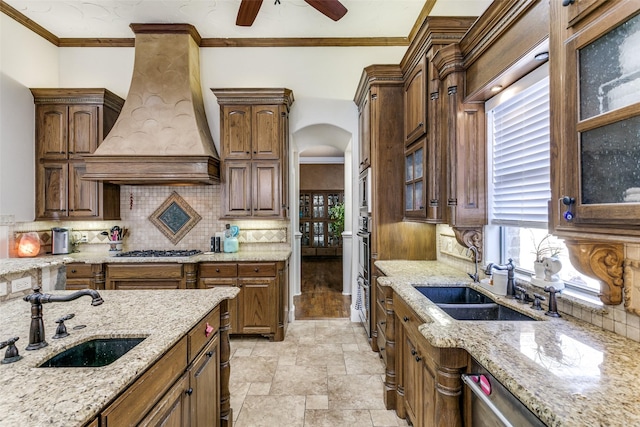 kitchen featuring decorative backsplash, sink, light stone counters, and custom range hood