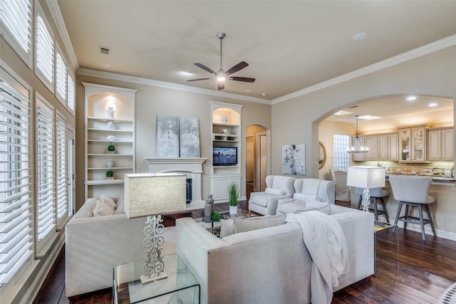 living room with ceiling fan, built in features, dark wood-type flooring, and crown molding