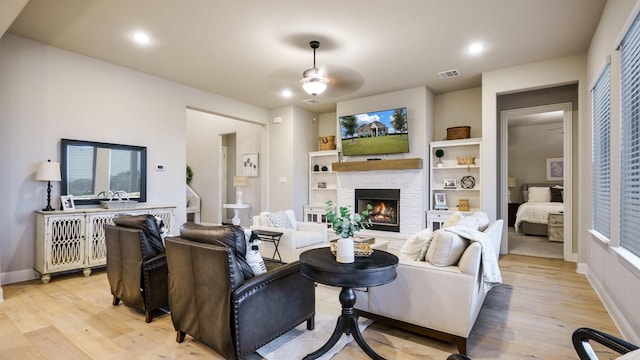 living room featuring ceiling fan, built in shelves, a fireplace, and light hardwood / wood-style flooring