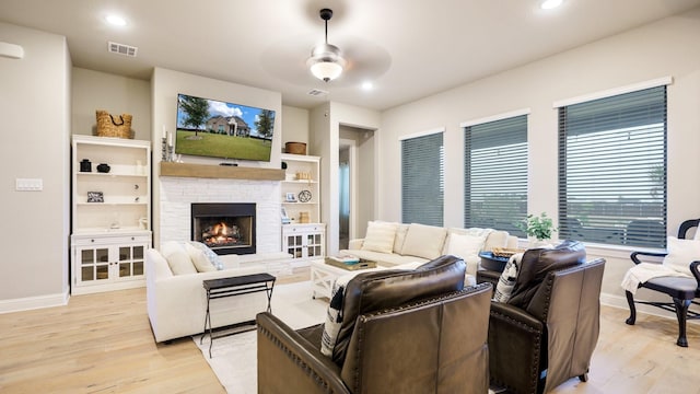 living room with ceiling fan, a stone fireplace, and light hardwood / wood-style flooring