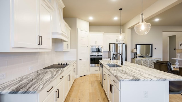 kitchen featuring pendant lighting, appliances with stainless steel finishes, white cabinetry, sink, and a center island with sink