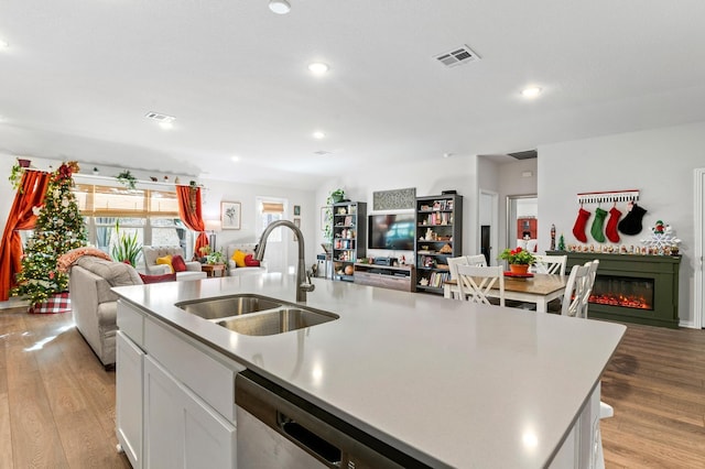 kitchen with light hardwood / wood-style floors, sink, white cabinetry, and a center island with sink