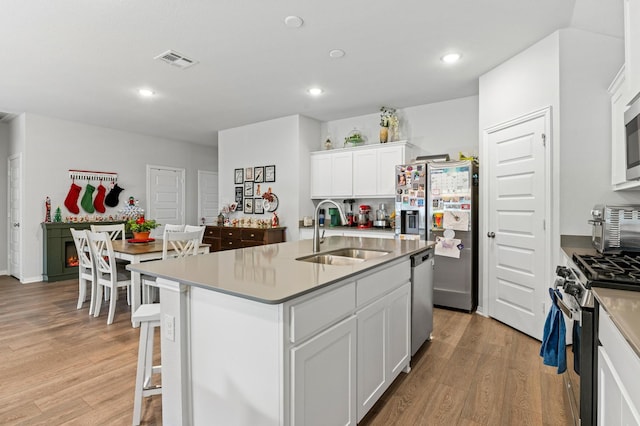 kitchen with white cabinetry, stainless steel appliances, sink, light wood-type flooring, and a center island with sink