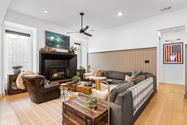 living room featuring ceiling fan, light hardwood / wood-style floors, and a tile fireplace