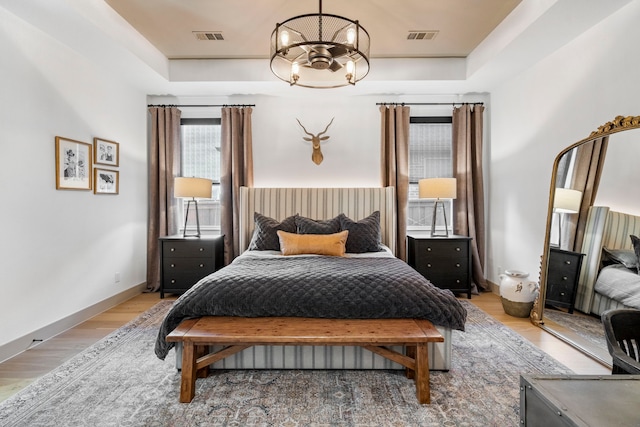 bedroom with light wood-type flooring, a chandelier, and a raised ceiling