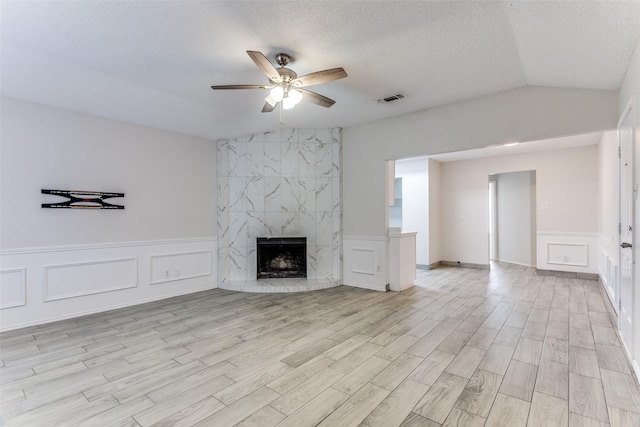 unfurnished living room with ceiling fan, vaulted ceiling, a fireplace, light hardwood / wood-style floors, and a textured ceiling