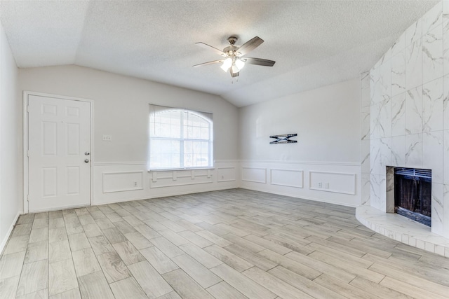 interior space with ceiling fan, light wood-type flooring, lofted ceiling, a textured ceiling, and a high end fireplace