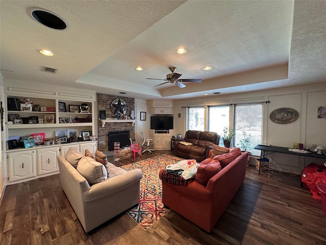 living room featuring a tray ceiling, dark hardwood / wood-style flooring, a fireplace, a textured ceiling, and built in shelves