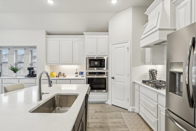 kitchen with stainless steel appliances, a sink, white cabinetry, and custom range hood