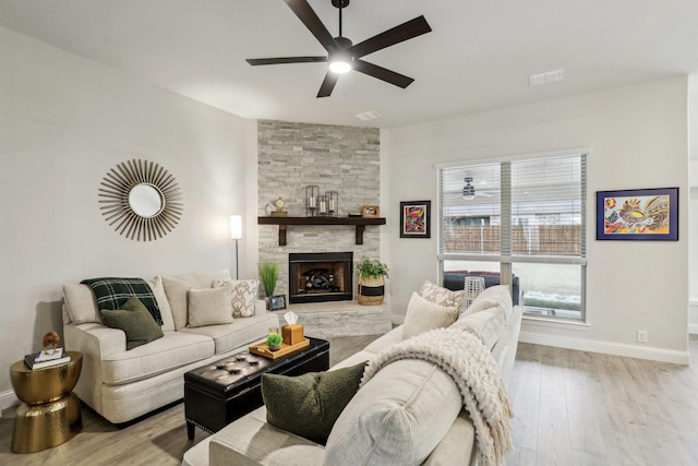 living room featuring ceiling fan, light hardwood / wood-style flooring, and a stone fireplace