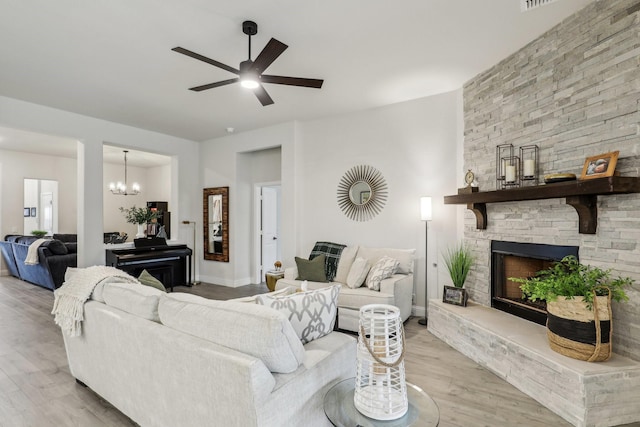 living room with light wood-type flooring, ceiling fan with notable chandelier, and a stone fireplace