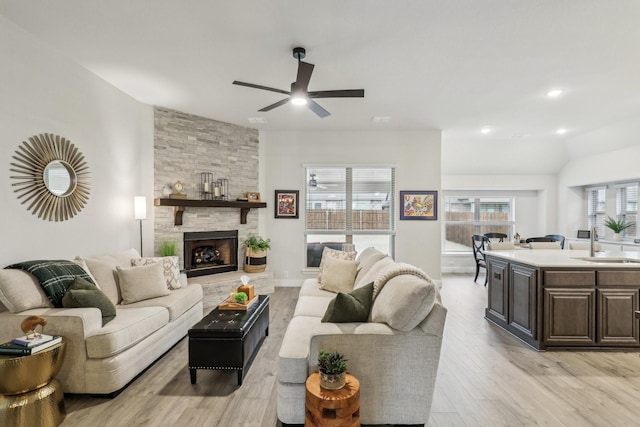 living room with ceiling fan, light hardwood / wood-style flooring, a stone fireplace, and sink