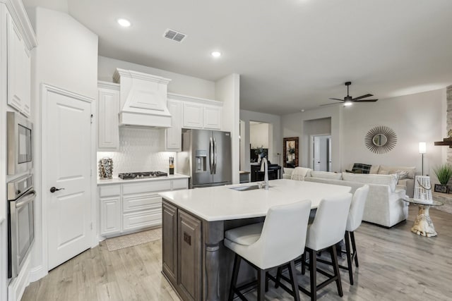 kitchen featuring stainless steel appliances, sink, white cabinetry, and custom range hood