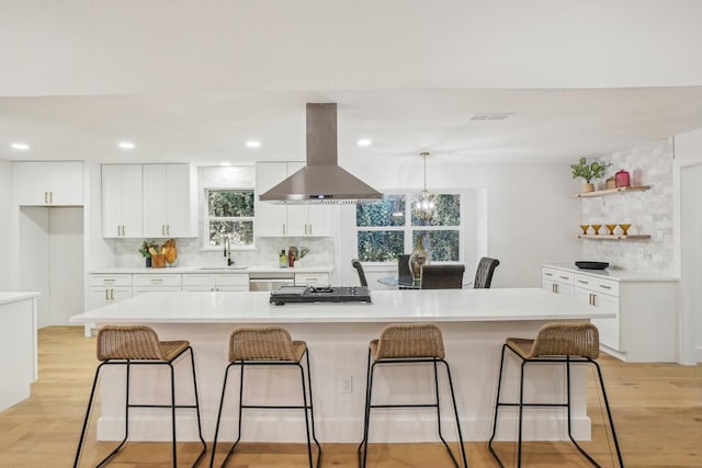 kitchen featuring light hardwood / wood-style flooring, a large island, island exhaust hood, backsplash, and white cabinets