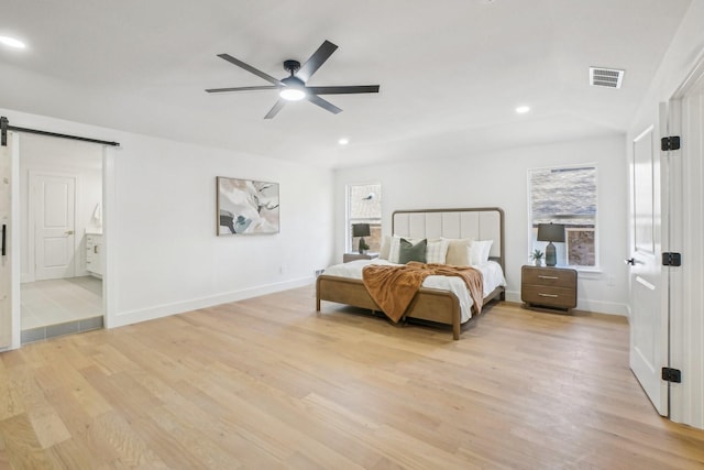 bedroom featuring ceiling fan, connected bathroom, a barn door, and light wood-type flooring