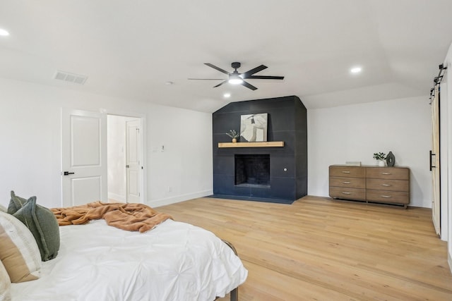 bedroom featuring ceiling fan, a tile fireplace, lofted ceiling, and light wood-type flooring