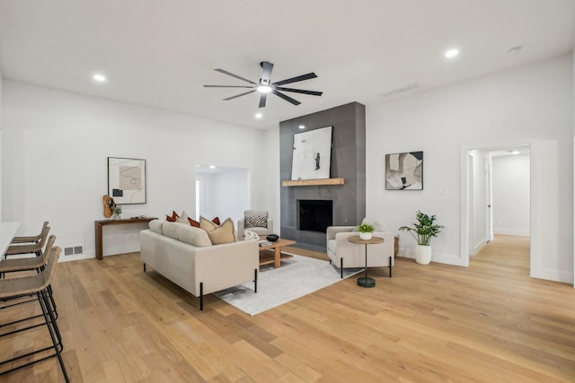 living room with ceiling fan, a large fireplace, and light hardwood / wood-style floors