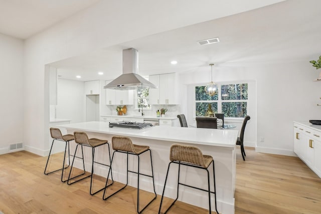 kitchen featuring decorative light fixtures, island exhaust hood, white cabinetry, and light hardwood / wood-style flooring