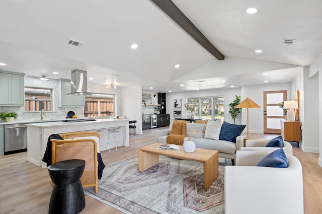 living room featuring sink, light hardwood / wood-style flooring, and vaulted ceiling with beams