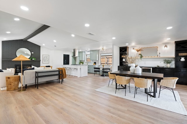 dining space with a fireplace, light hardwood / wood-style flooring, and lofted ceiling with beams