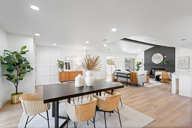 dining area featuring lofted ceiling, a brick fireplace, and light hardwood / wood-style flooring