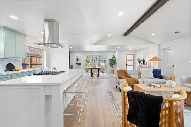 kitchen featuring island exhaust hood, vaulted ceiling with beams, stainless steel gas cooktop, light wood-type flooring, and green cabinets