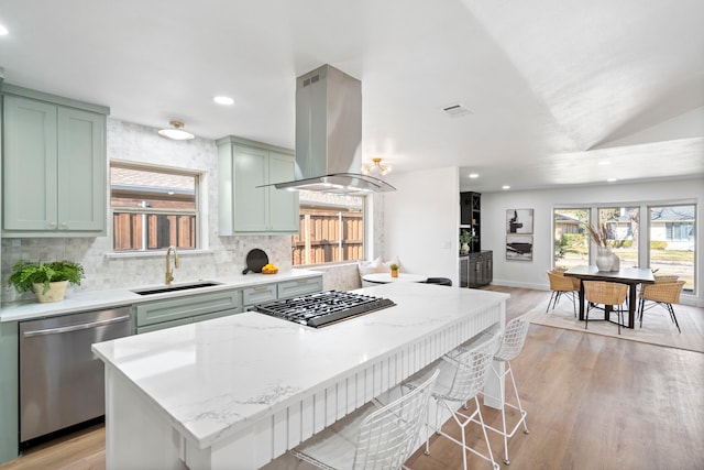 kitchen featuring island range hood, stainless steel appliances, green cabinetry, light stone counters, and sink