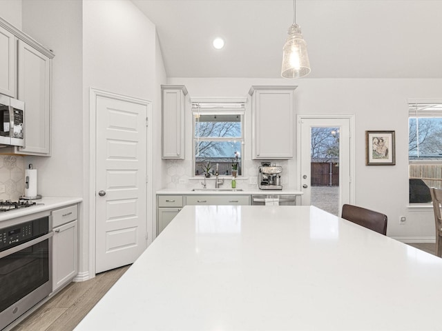 kitchen with appliances with stainless steel finishes, backsplash, light wood-type flooring, pendant lighting, and sink