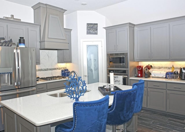 kitchen featuring appliances with stainless steel finishes, custom exhaust hood, tasteful backsplash, and a kitchen island with sink