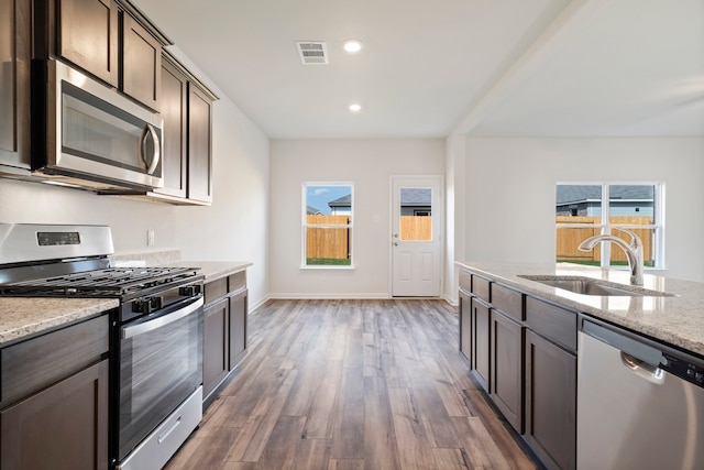 kitchen featuring light stone countertops, appliances with stainless steel finishes, dark brown cabinets, and sink