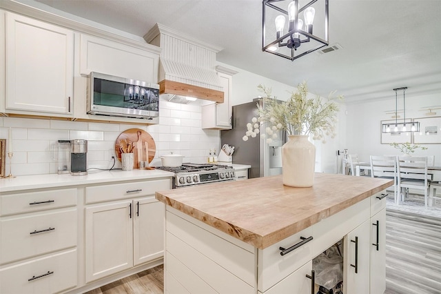 kitchen featuring butcher block counters, white cabinetry, stainless steel appliances, a center island, and decorative light fixtures