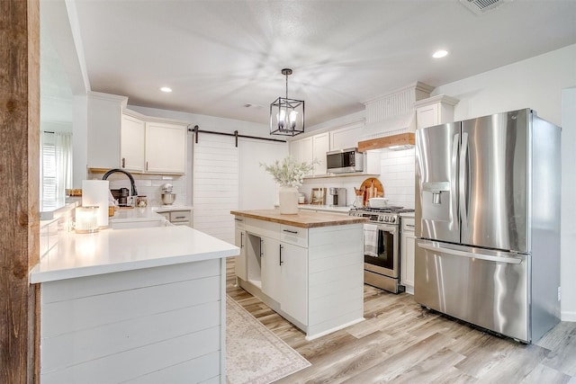 kitchen featuring decorative backsplash, a barn door, white cabinets, and appliances with stainless steel finishes