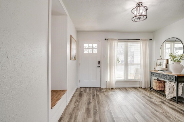 entrance foyer with light hardwood / wood-style floors, a textured ceiling, and an inviting chandelier