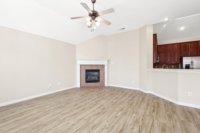 unfurnished living room with lofted ceiling, ceiling fan, a tile fireplace, and light hardwood / wood-style flooring