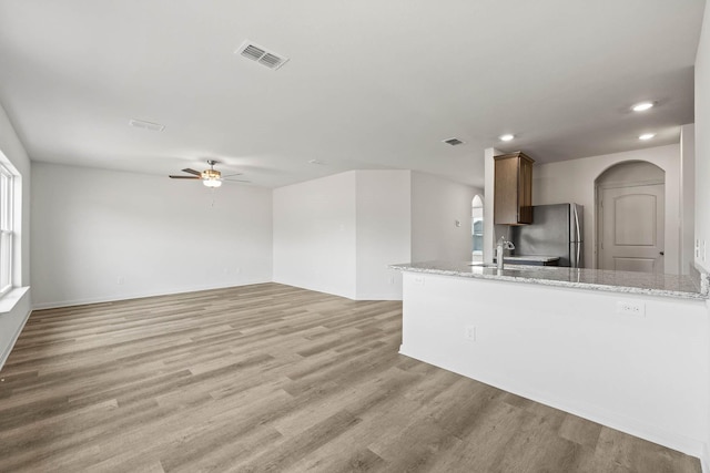 kitchen with light stone countertops, sink, stainless steel fridge, ceiling fan, and light hardwood / wood-style flooring