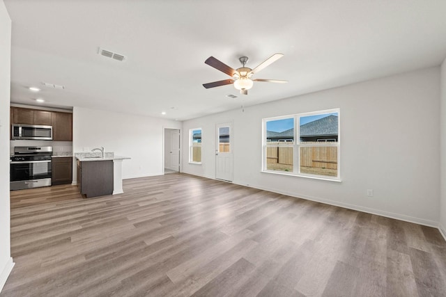 unfurnished living room with ceiling fan, light wood-type flooring, and sink