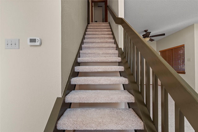 stairs featuring ceiling fan and a textured ceiling