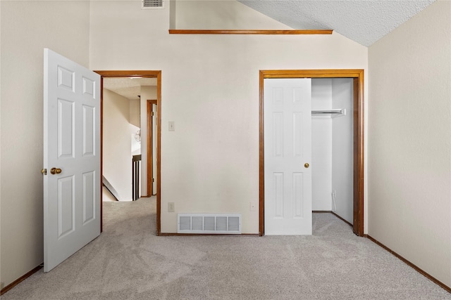 unfurnished bedroom with lofted ceiling, light colored carpet, a closet, and a textured ceiling