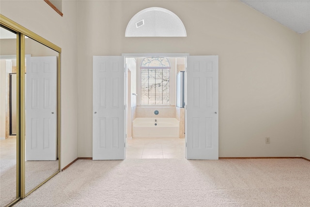 unfurnished bedroom featuring high vaulted ceiling, connected bathroom, a closet, and light carpet