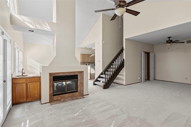 unfurnished living room featuring ceiling fan, a tiled fireplace, light colored carpet, high vaulted ceiling, and sink