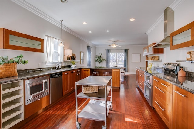 kitchen with stainless steel appliances, hanging light fixtures, ornamental molding, wall chimney exhaust hood, and a center island