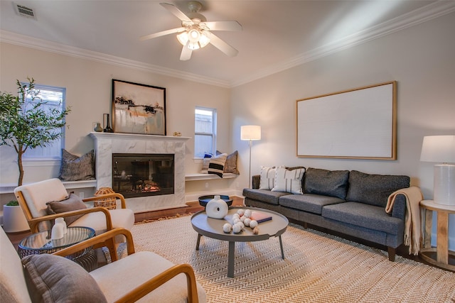 living room featuring ceiling fan, a high end fireplace, crown molding, and light hardwood / wood-style flooring