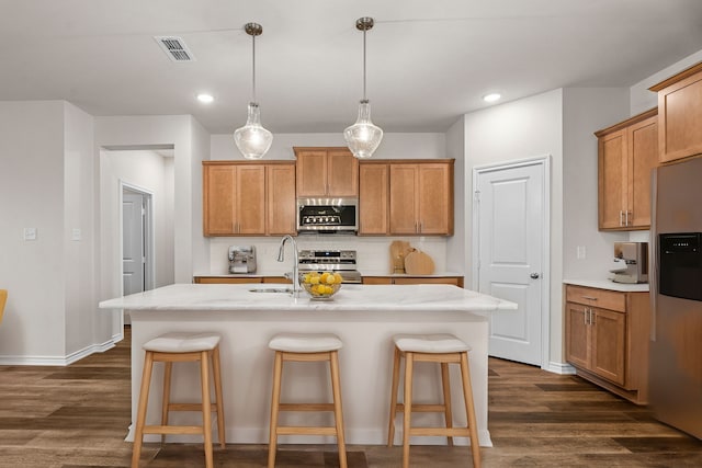 kitchen featuring dark wood-type flooring, appliances with stainless steel finishes, decorative light fixtures, and a kitchen island with sink