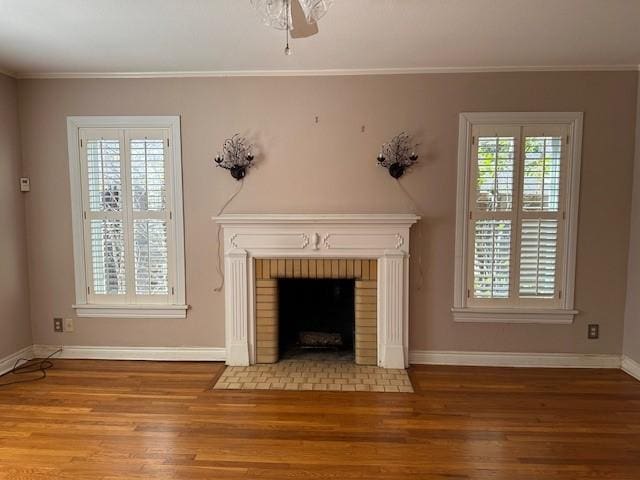 unfurnished living room with ceiling fan, wood-type flooring, a brick fireplace, and crown molding