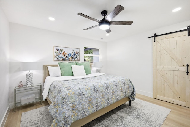 bedroom featuring ceiling fan, light hardwood / wood-style floors, and a barn door