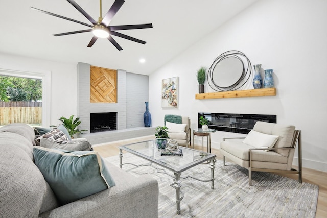 living room featuring lofted ceiling, light wood-type flooring, a fireplace, and ceiling fan